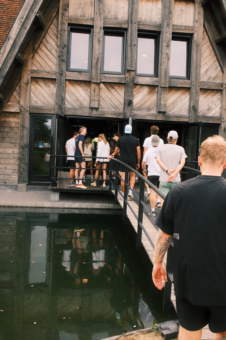Groep sporters loopt over een brug naar een houten gebouw